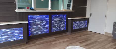 Een modern ontworpen receptiegedeelte met een houten vloer en een receptiebalie met een digitaal scherm.