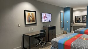 A hotel room with a desk, chair, two beds, a TV, and a bathroom mirror. - Haven Inn & Suites Downtown Houston (Houston)