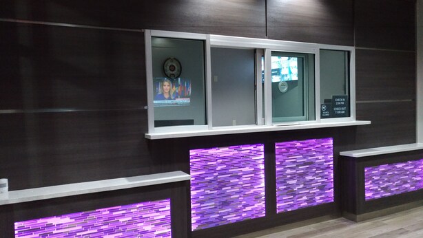 A reception area with a modern design, featuring a reception desk with a digital display, purple illuminated panels, and a dark wood finish wall. - Haven Inn & Suites Downtown Houston (Houston)