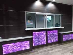 A reception area with a modern design, featuring a reception desk with a digital display, purple illuminated panels, and a dark wood finish wall. - Haven Inn & Suites Downtown Houston (Houston)