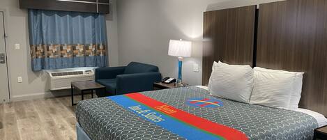 A hotel room with a bed, a desk, a chair, a lamp, and a window with curtains.