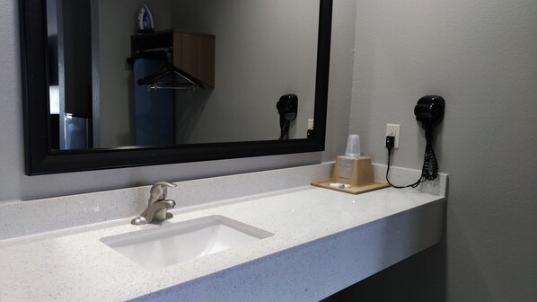 A bathroom with a white sink, a mirror, a hairdryer, and a telephone. - Haven Inn & Suites Downtown Houston (Houston)