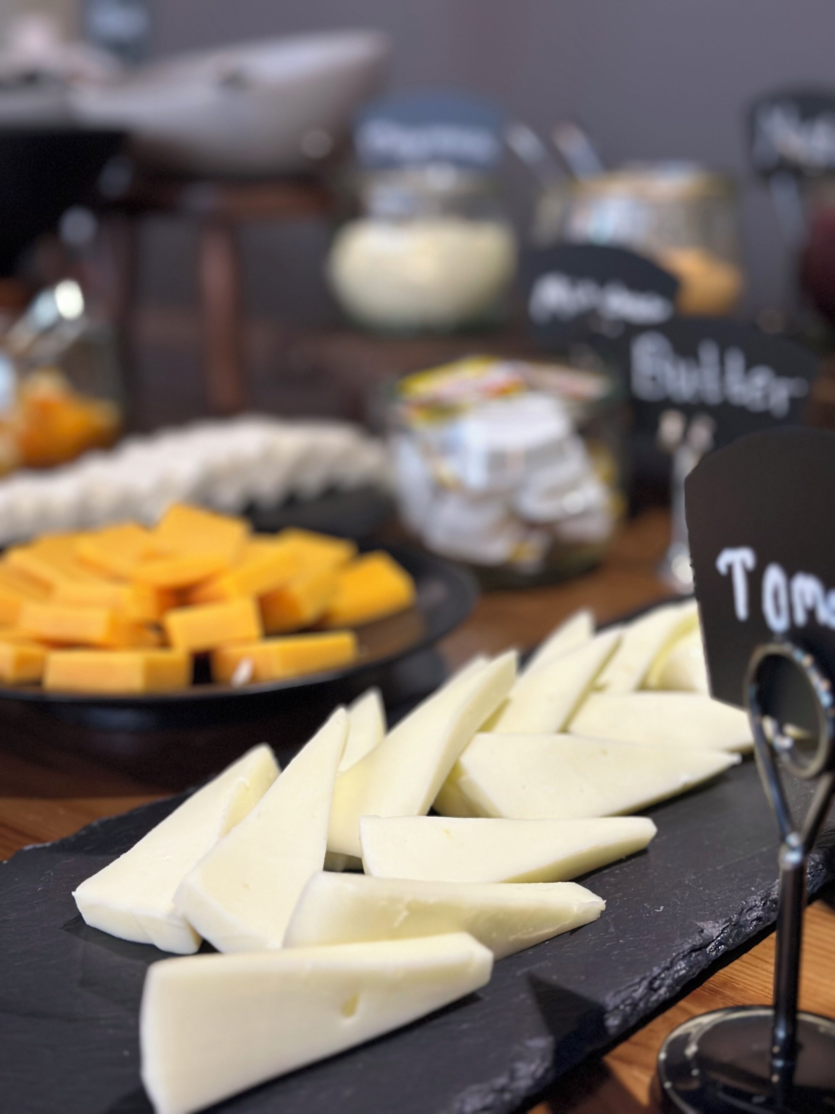 Una tabla de quesos con distintos tipos de queso y un cartel que dice 'Tom'.