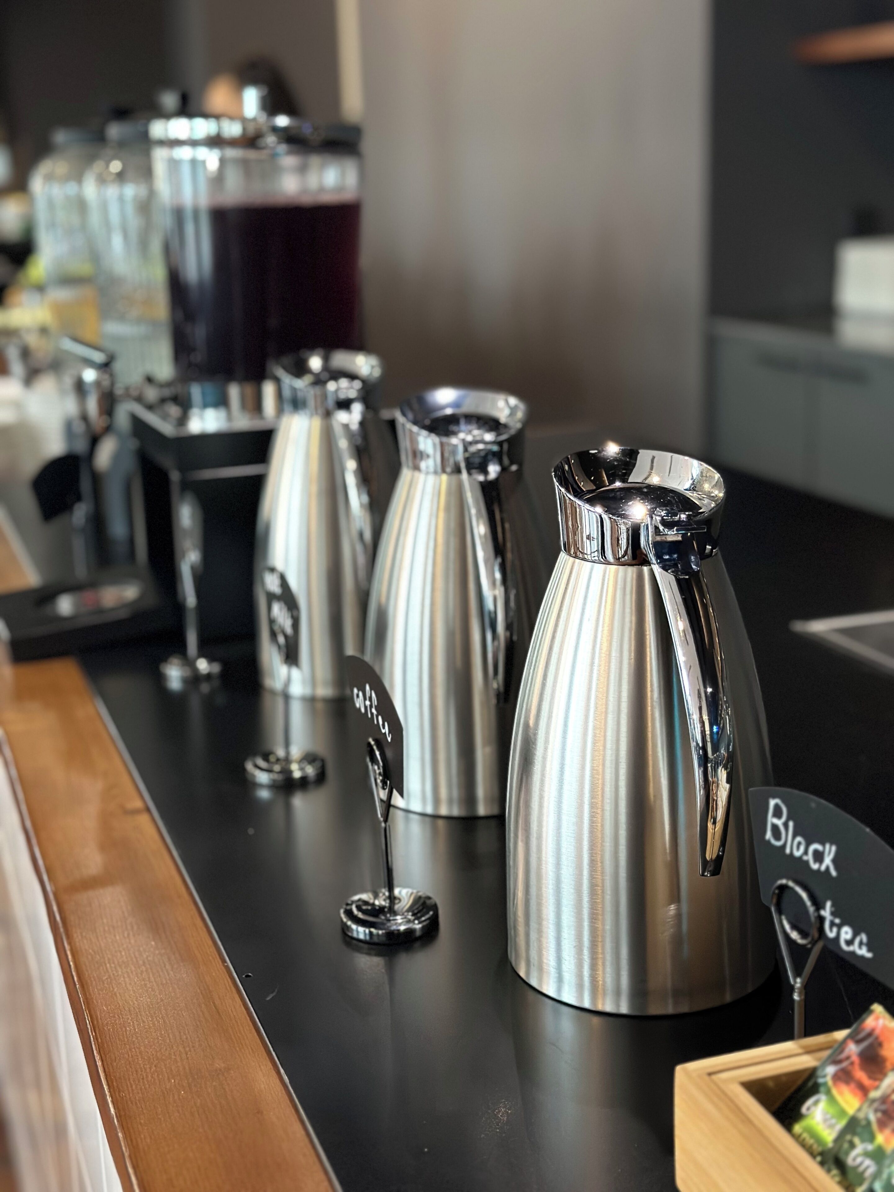 Een koffiehoek met verschillende roestvrijstalen koffiezetapparaten en een bordje met de tekst 'Black Tea'.