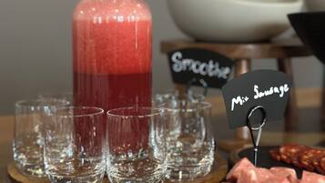 En buffetbod med en kande rød smoothie, flere glas og en tallerken med skåret kød.