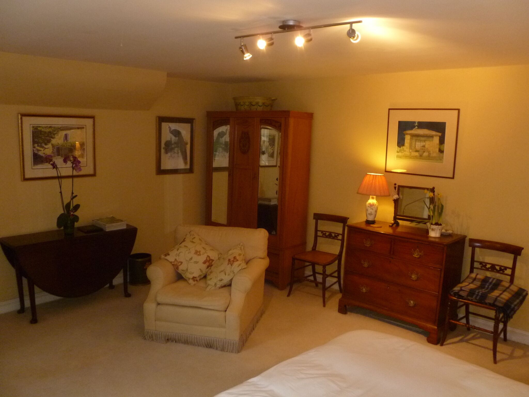 A bedroom with a bed, a chair, a dresser, a desk, and a mirror.