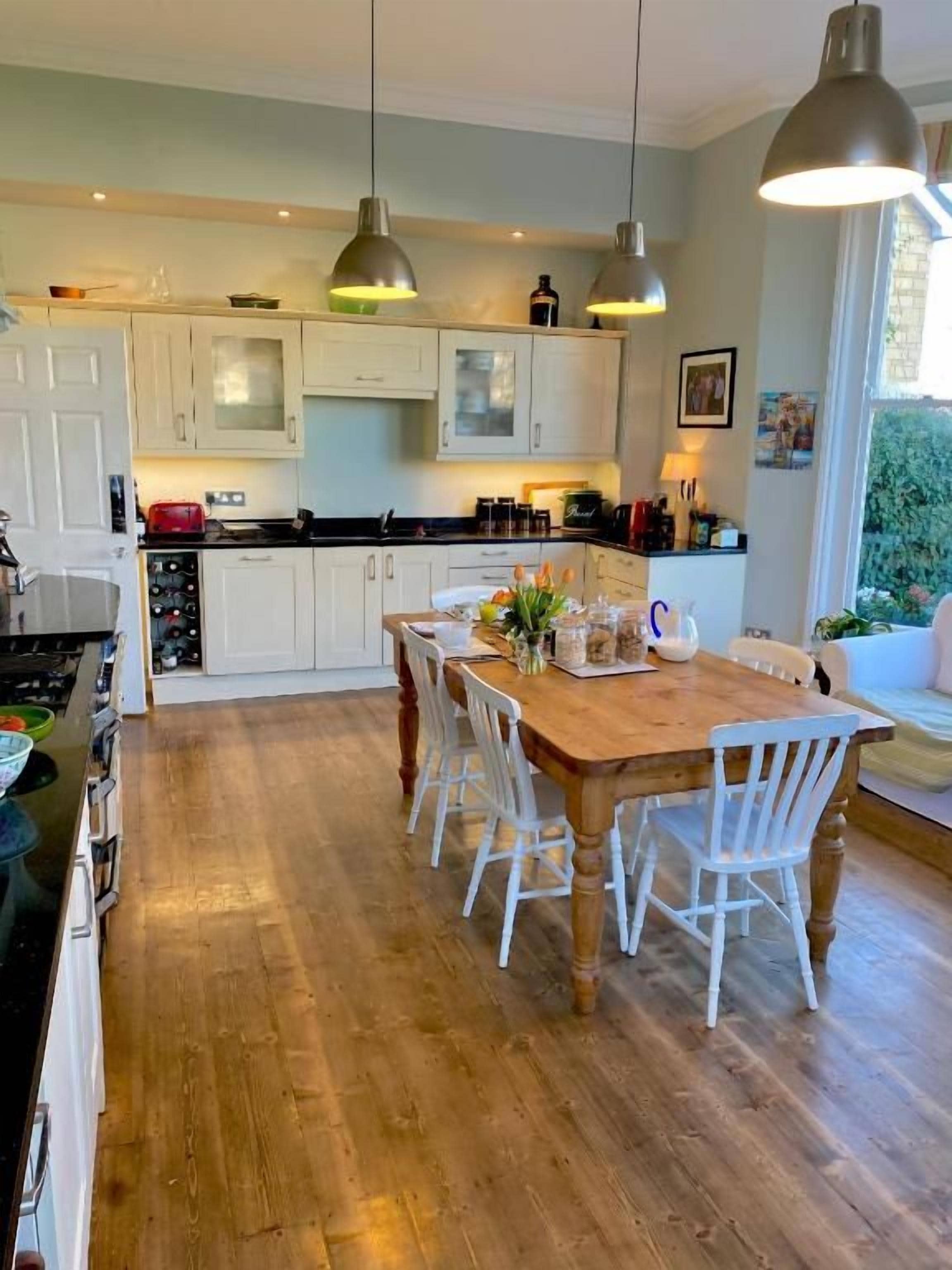 Een keuken met houten kasten, een eettafel met stoelen, hanglampen en uitzicht op groen.