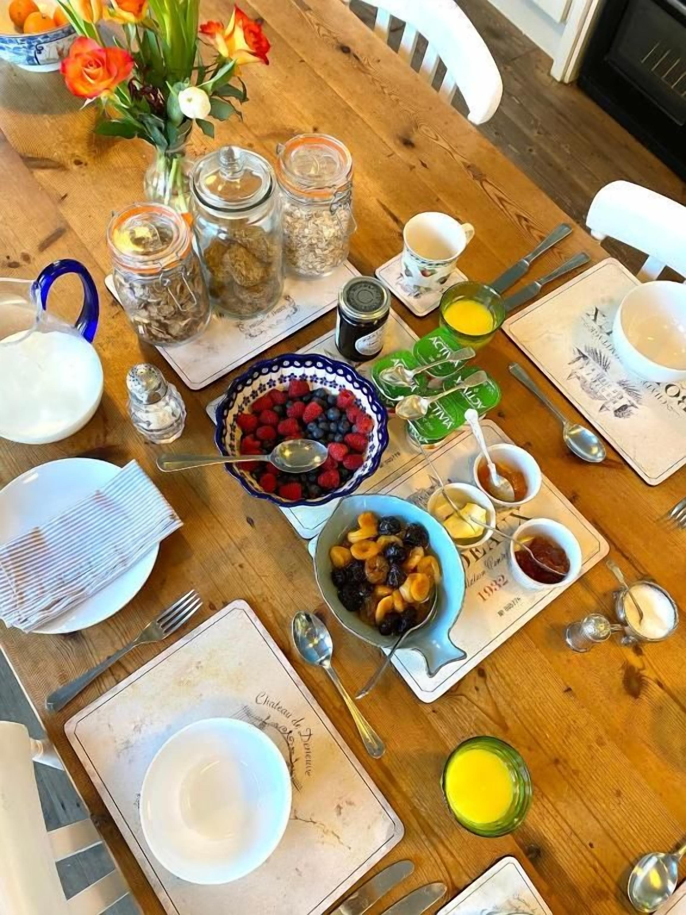 Una mesa de comedor de madera dispuesta con varios platos, incluyendo un bol de bayas, un plato de huevos y varios frascos pequeños.