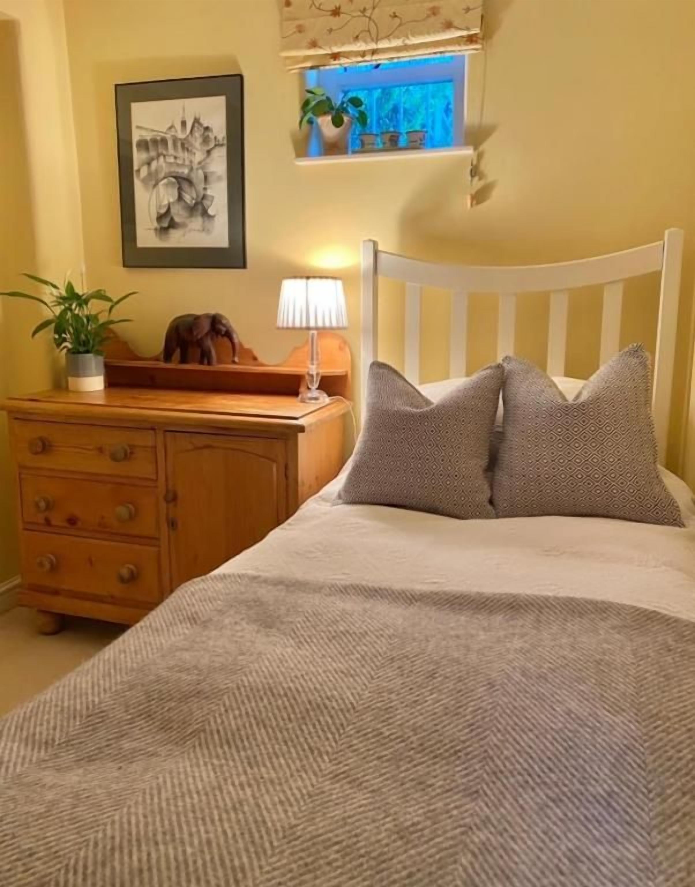 Una camera da letto con un letto, un comodino, una cassettiera, una lampada e un quadro appeso al muro.