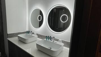 Un baño moderno con dos lavamanos, un espejo grande y luces circulares sobre los espejos.