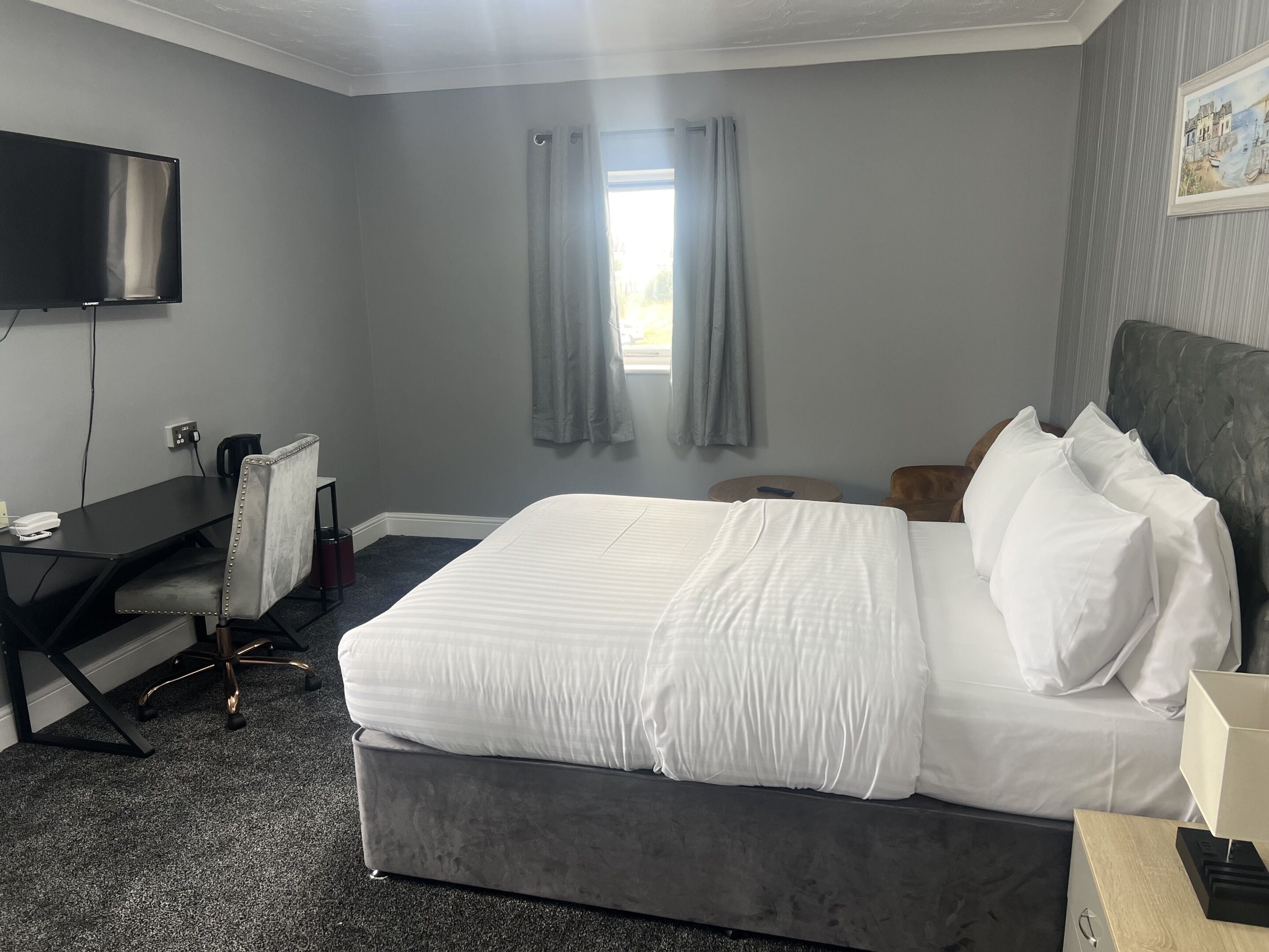 A hotel room with a bed, a desk with a chair, a television, and a window with curtains.
