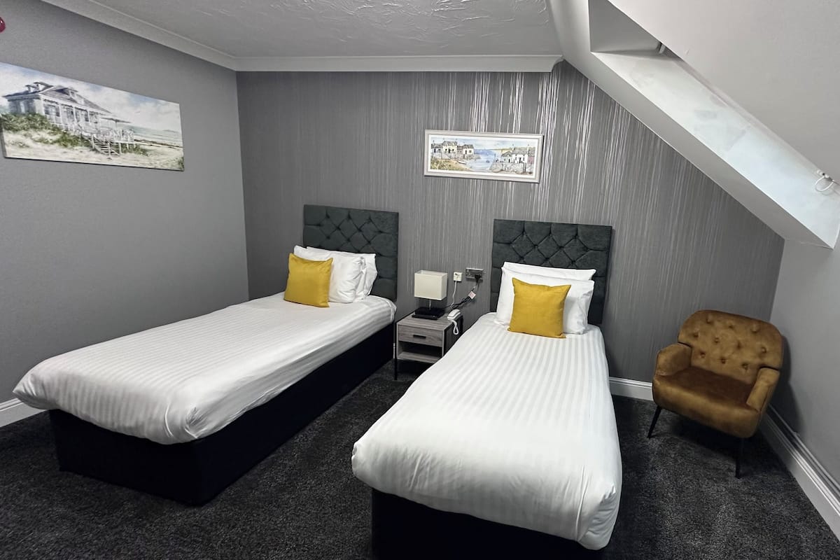 A hotel room with two single beds, a nightstand, a chair, and a framed picture on the wall.