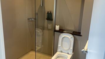 Un baño moderno con ducha de vidrio, inodoro y estante con artículos de aseo.
