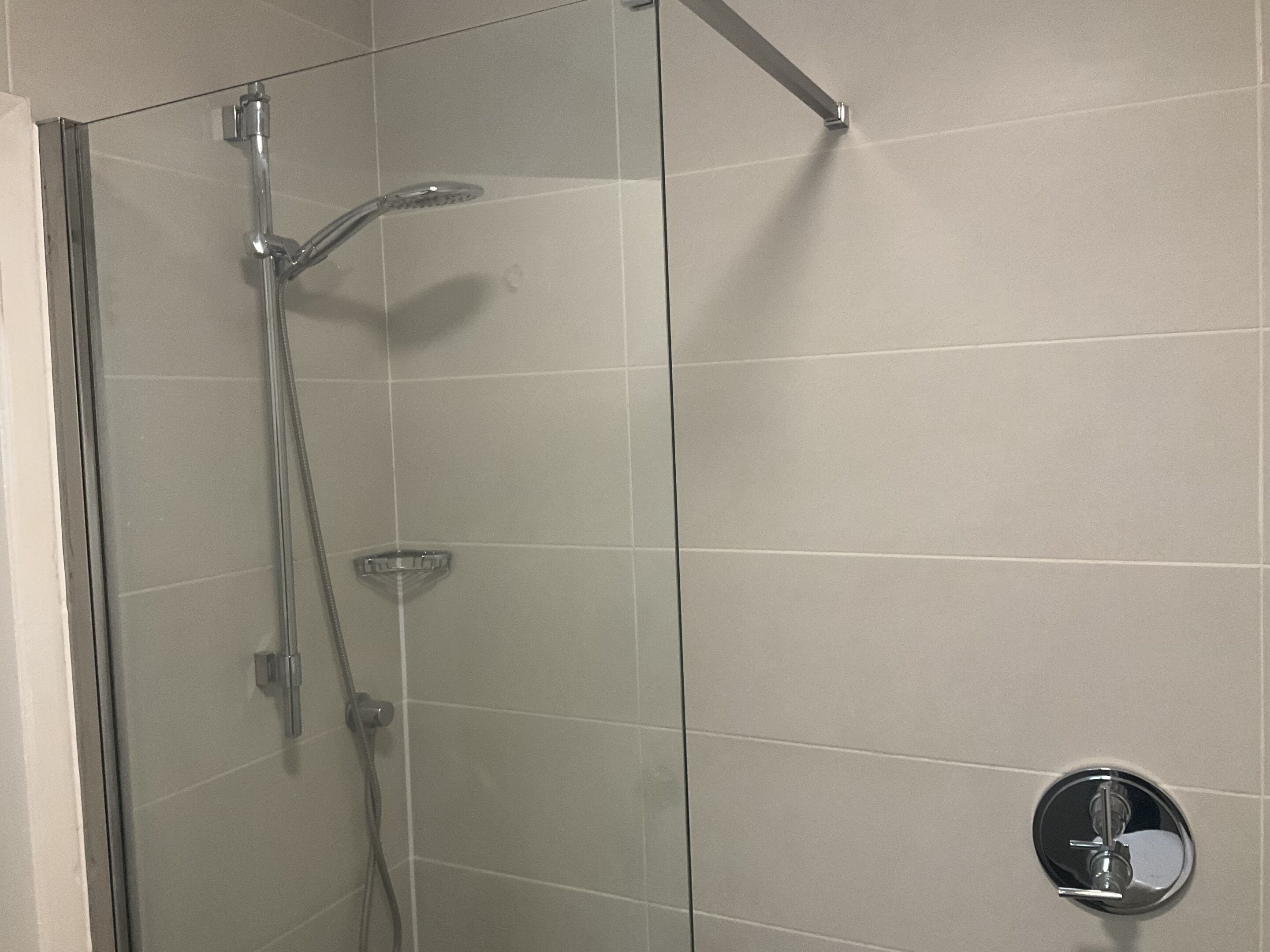 A glass-enclosed shower with a handheld showerhead and a handheld faucet.
