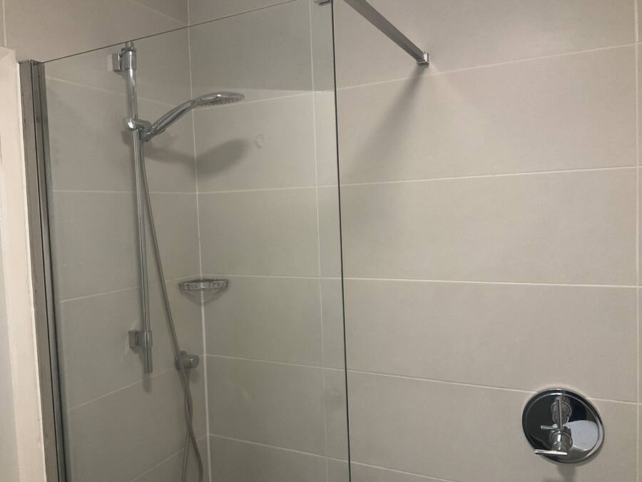 A glass-enclosed shower with a handheld showerhead and a handheld faucet.