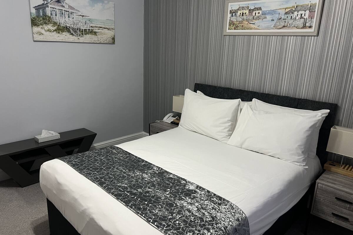 A hotel room with a bed, bedside tables, a nightstand, a lamp, and two framed pictures on the wall.