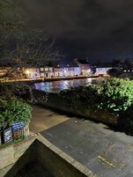 A nighttime view of a riverside town with buildings along the water, a pedestrian sign, and a sign for a coffee shop.