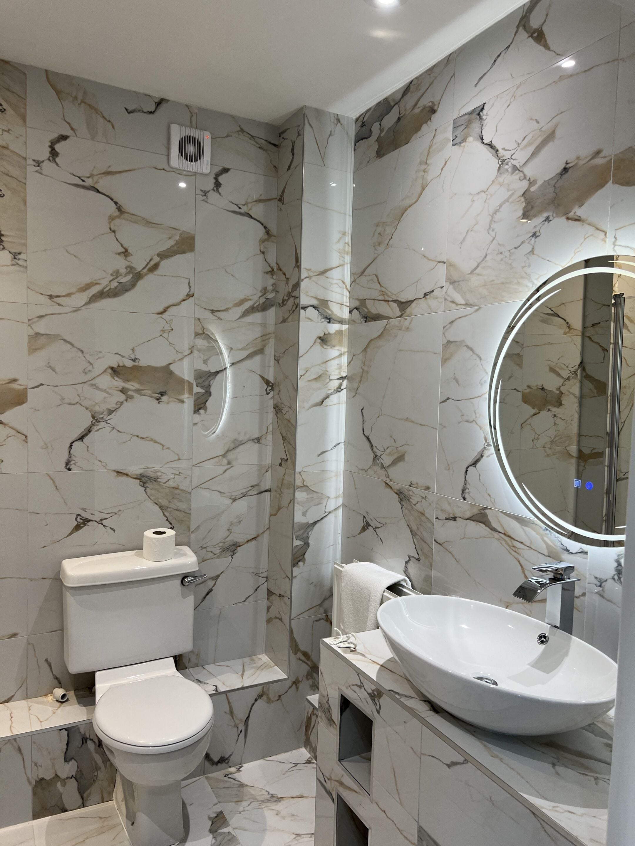 Une salle de bain moderne avec des murs en marbre, des toilettes, un lavabo et un miroir.