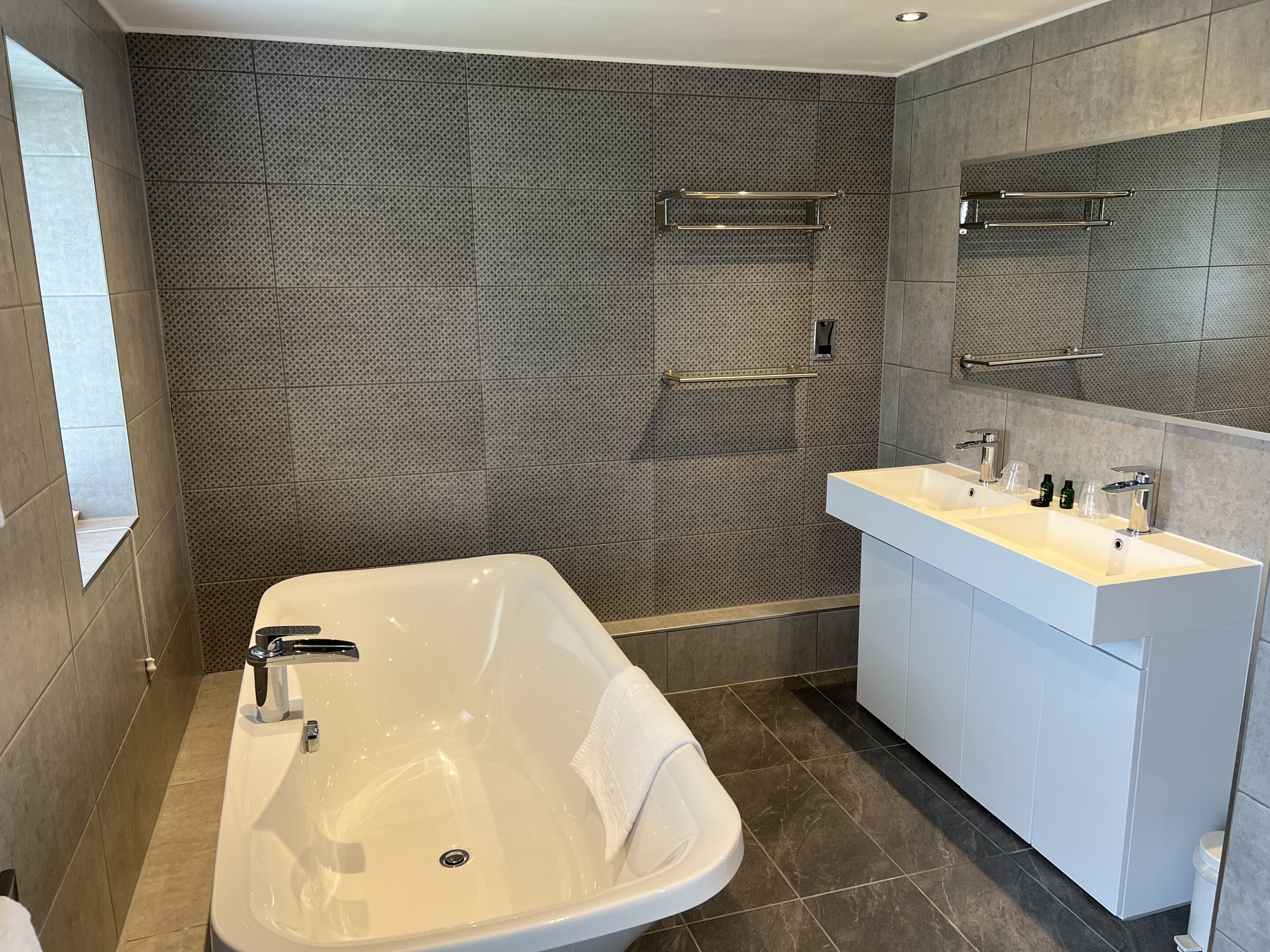 A modern bathroom with a freestanding bathtub, a white vanity with a large mirror, and a tiled shower area.