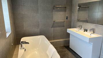 A modern bathroom with a freestanding bathtub, a white vanity with a large mirror, and a tiled shower area.