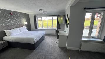 Una habitación de hotel moderna con una cama grande, un televisor de pantalla plana, un ventanal con vistas al exterior y una lámpara empotrada en el techo.