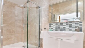 A modern bathroom with a glass shower enclosure, a white vanity with a sink, and a tiled backsplash. - Heritage Bed & Breakfast (Calne)