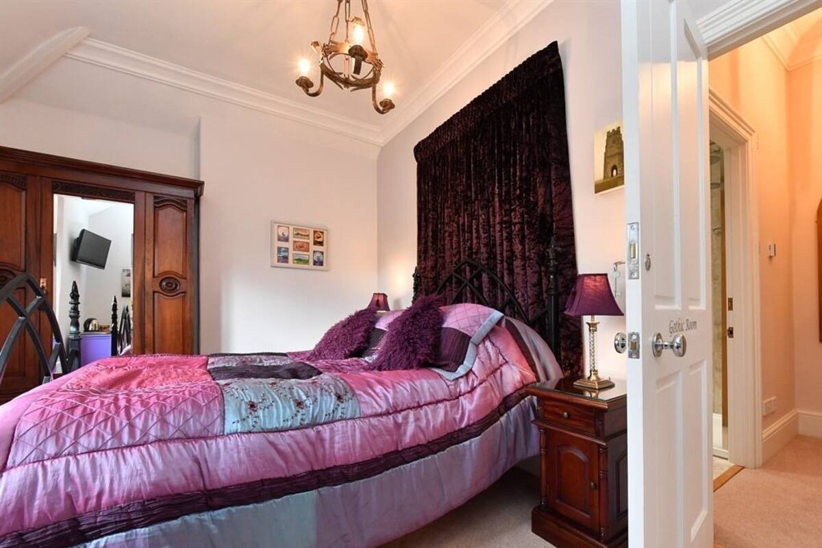 A bedroom with a large bed, a chandelier, a dark curtain, and a door labeled "Guest Room".