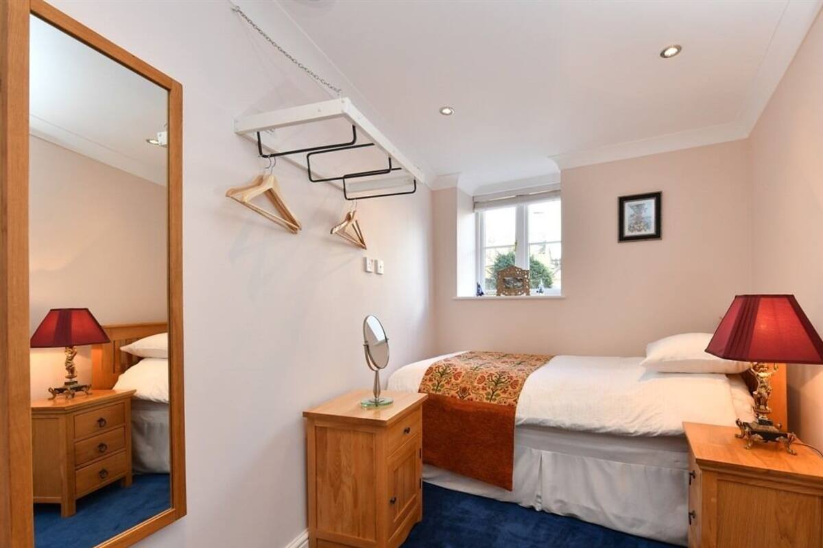A bedroom with a bed, two bedside tables, a mirror, a hanging clothes rack, and a window with a view of the outside.