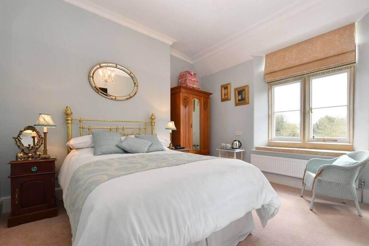 A bedroom with a large bed, a wooden wardrobe, a window with a view, and a chair.
