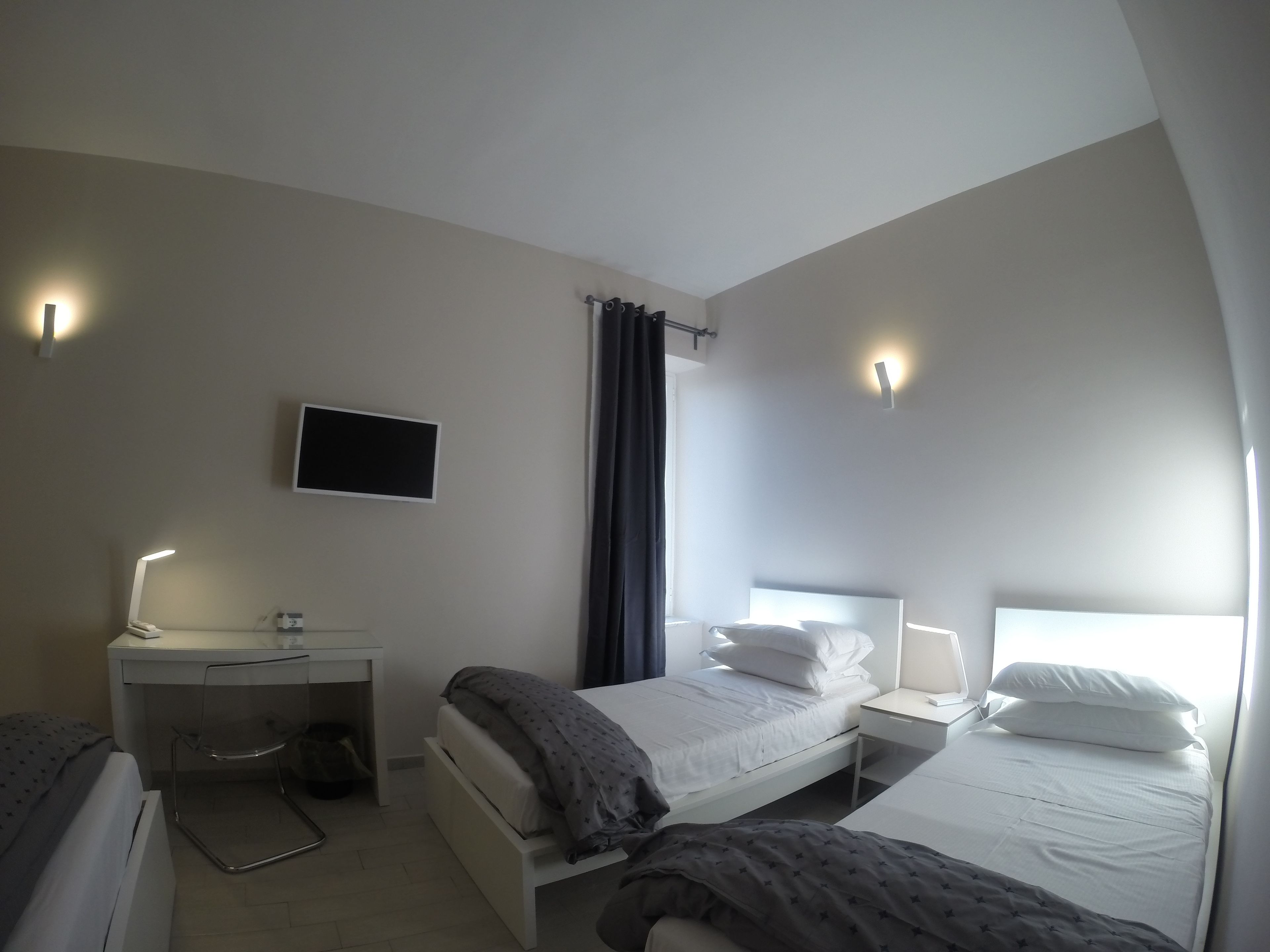 A modern hotel room with a bed, bedside tables, a desk, and a TV.