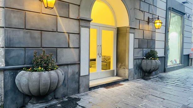 Une façade d’immeuble avec un revêtement extérieur en pierre, de grands pots de plantes et une entrée avec une porte en verre.