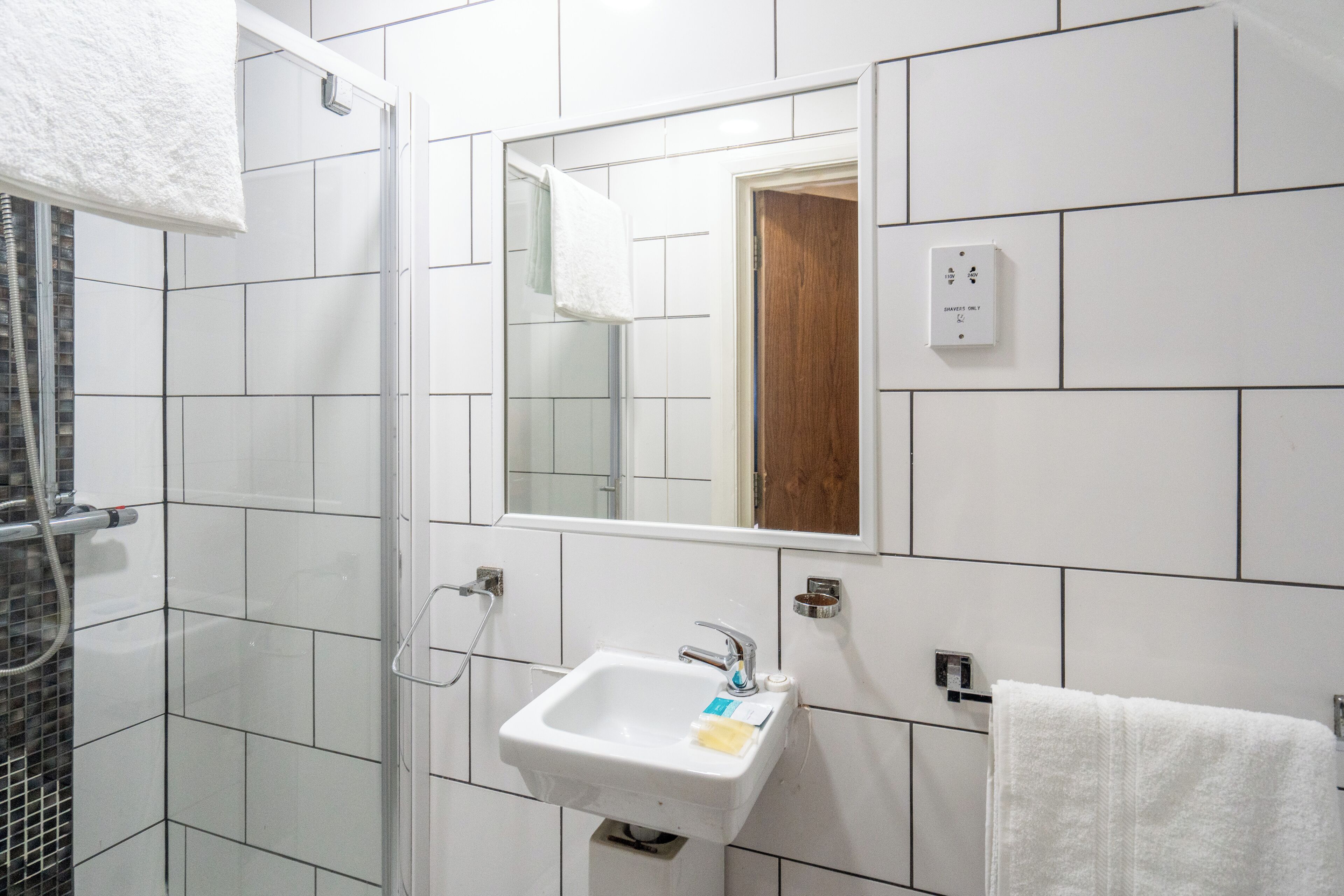 Un baño con ducha de vidrio, lavamanos con espejo y toalla colgada en la pared.