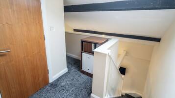A narrow hallway with a wooden door on the left, a white radiator on the right, and a small white cabinet against the wall.