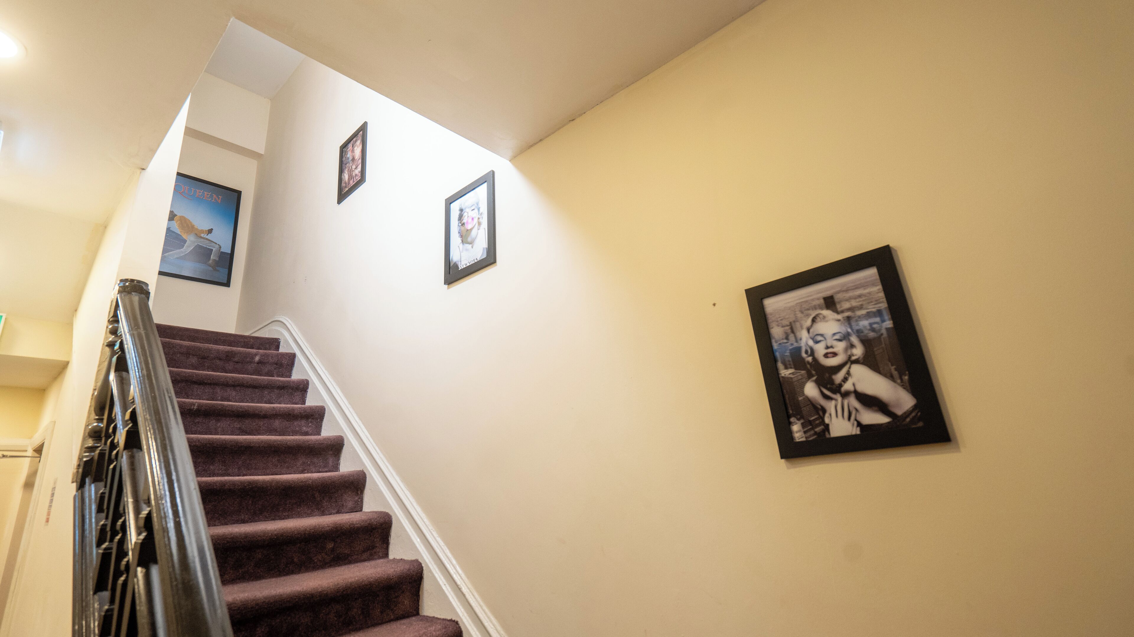 Un escalier avec une rampe, des murs de couleur beige et trois tableaux encadrés.