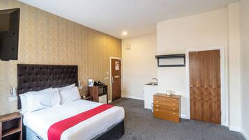 Ein Hotelzimmer mit einem großen Bett, einer Holzkommode, einem Schreibtisch mit Computer, einem kleinen Waschbecken und einem Kleiderschrank.