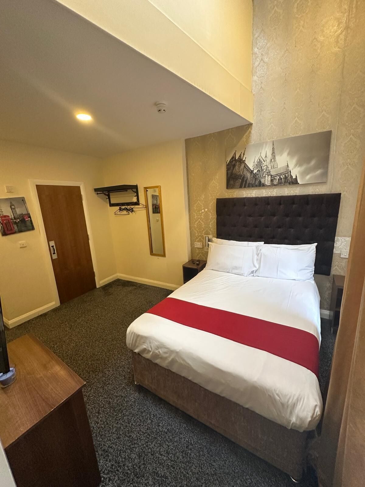 Een hotelkamer met een groot bed, een hoofdeinde, een nachtkastje, een spiegel en een deur.