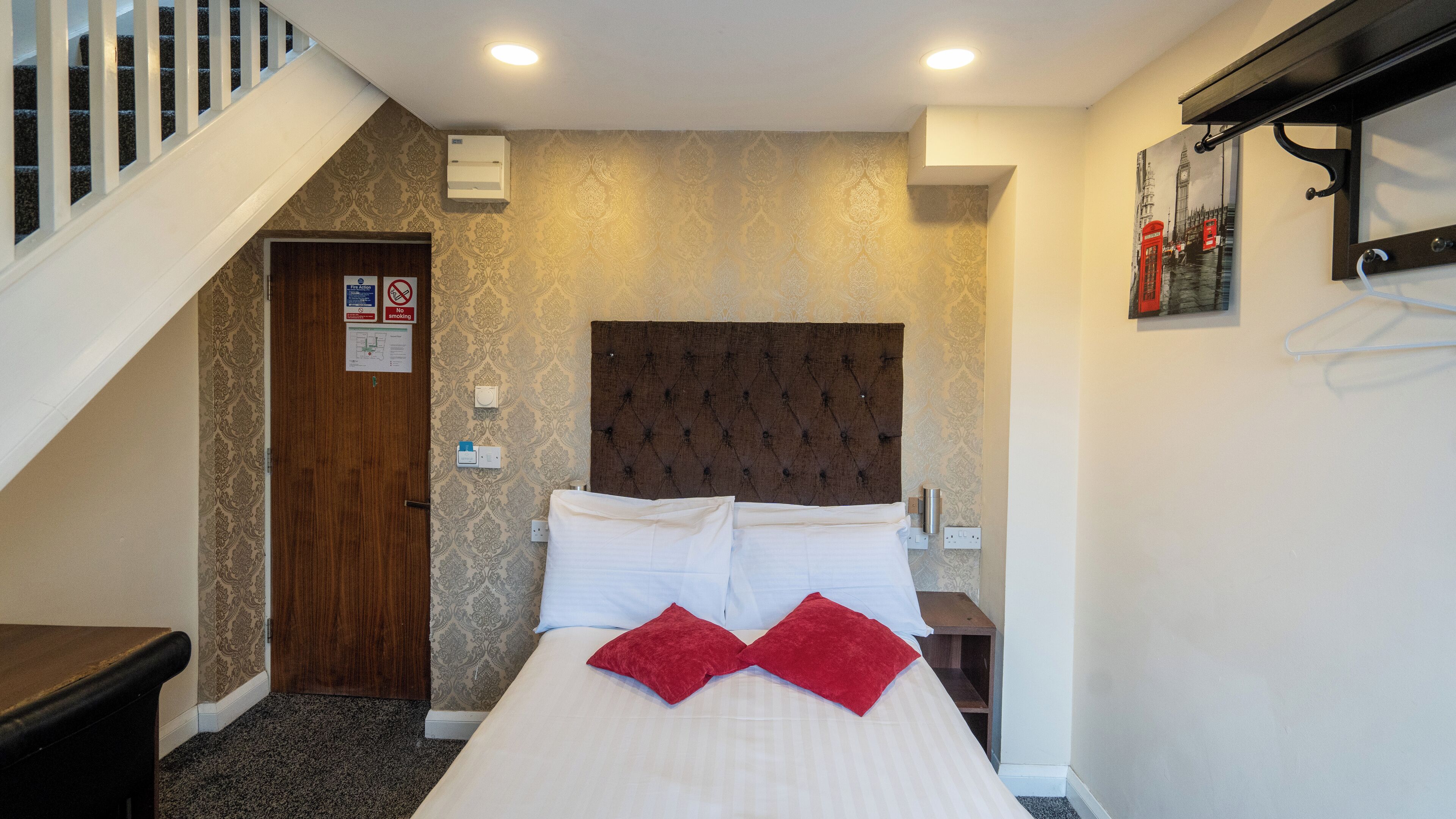 A hotel room with a bed, a wooden door, a staircase, and a wall with a patterned wallpaper.
