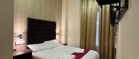 A hotel room with a large bed, a bedside table, a desk, and a wall-mounted TV.