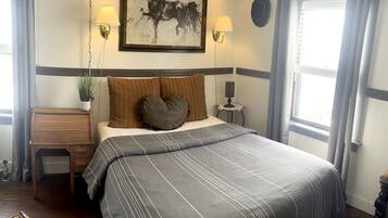 A neatly arranged bedroom with a large bed, two wall-mounted lamps, a framed horse painting, and a small table with a lamp.