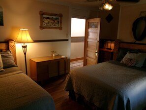 A bedroom with two beds, a bedside table, a lamp, a painting on the wall, and a wooden door. - Hotel Eastin (Kremmling)