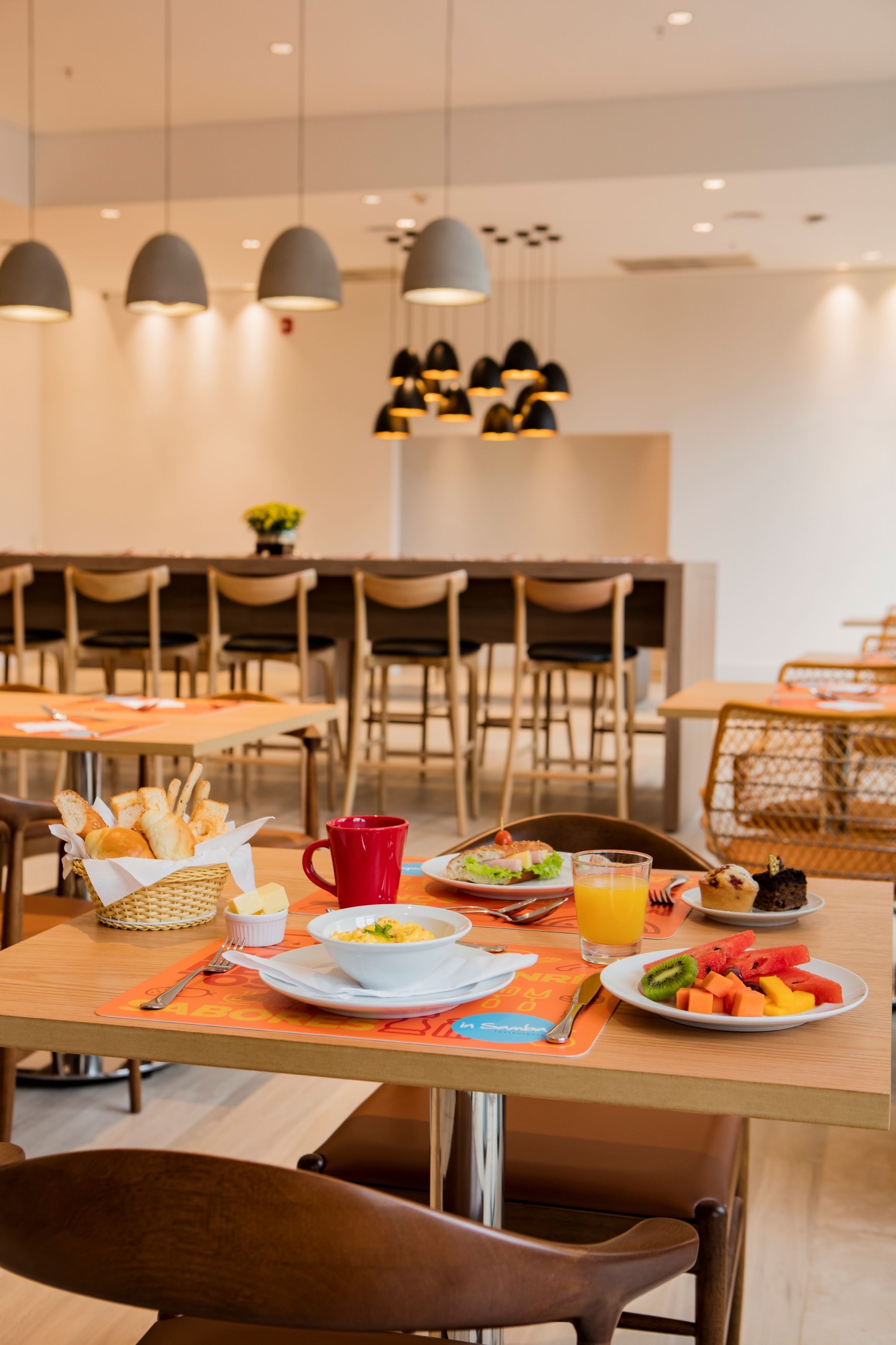 A dining area with tables set for breakfast, including plates of food, a red mug, and a basket of bread.