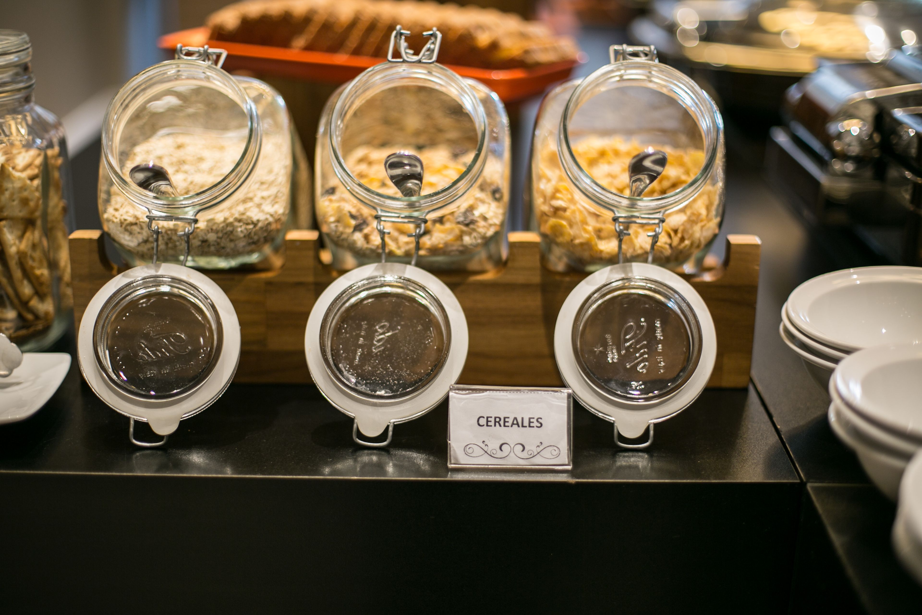 Un bufé de desayuno con diversas opciones de cereales exhibidas en frascos de vidrio.