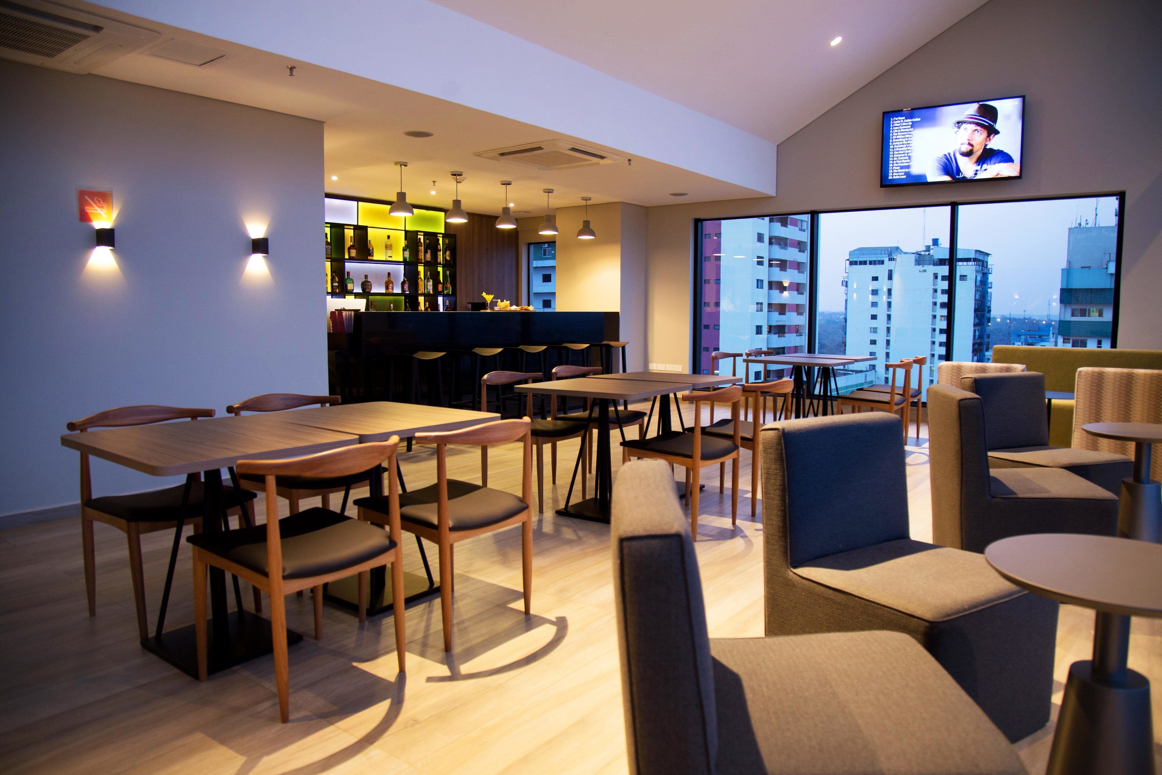 A modern hotel lobby with a bar area, seating arrangements, and a large window offering a city view.