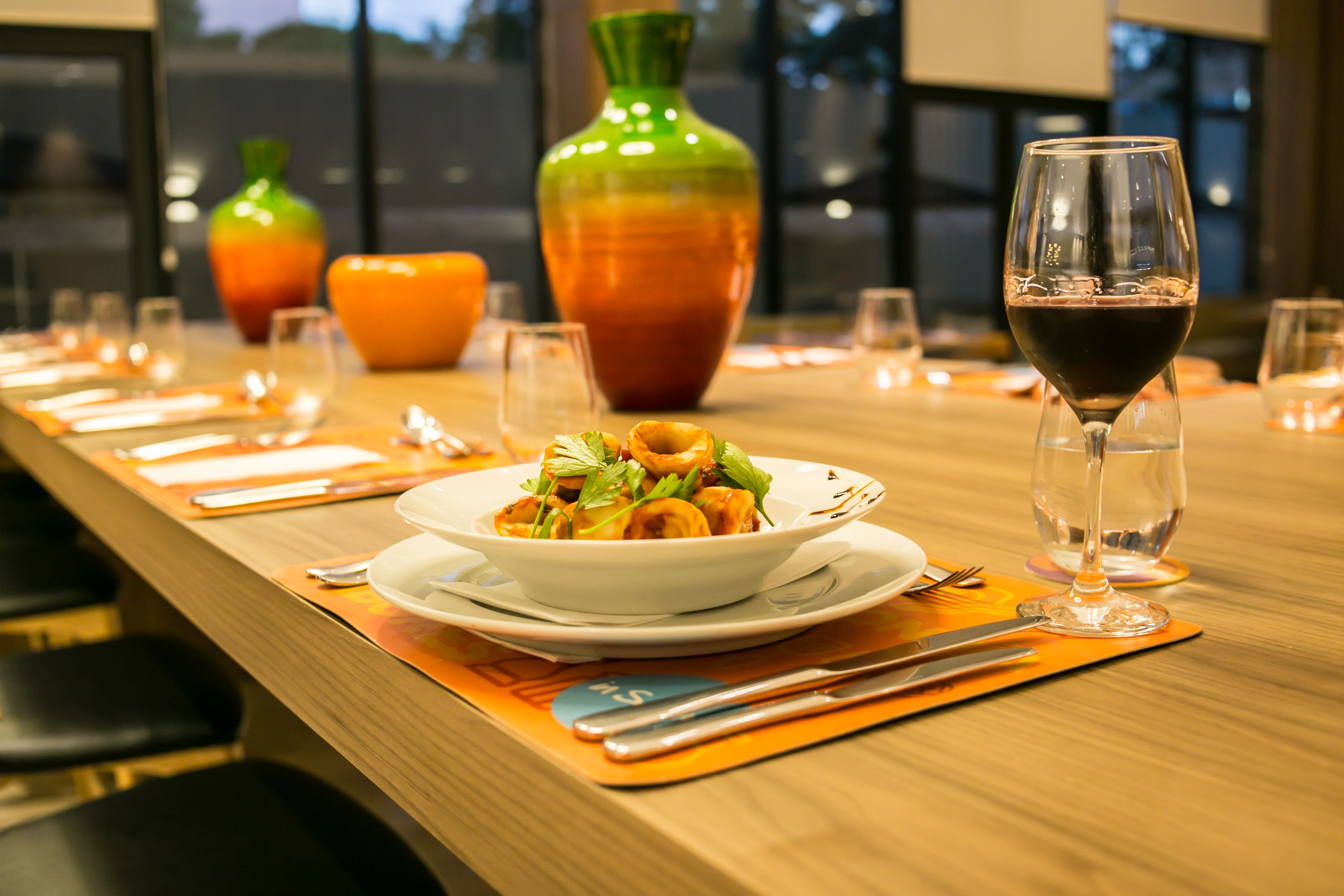 A dining table set with plates, cutlery, and a glass of red wine.