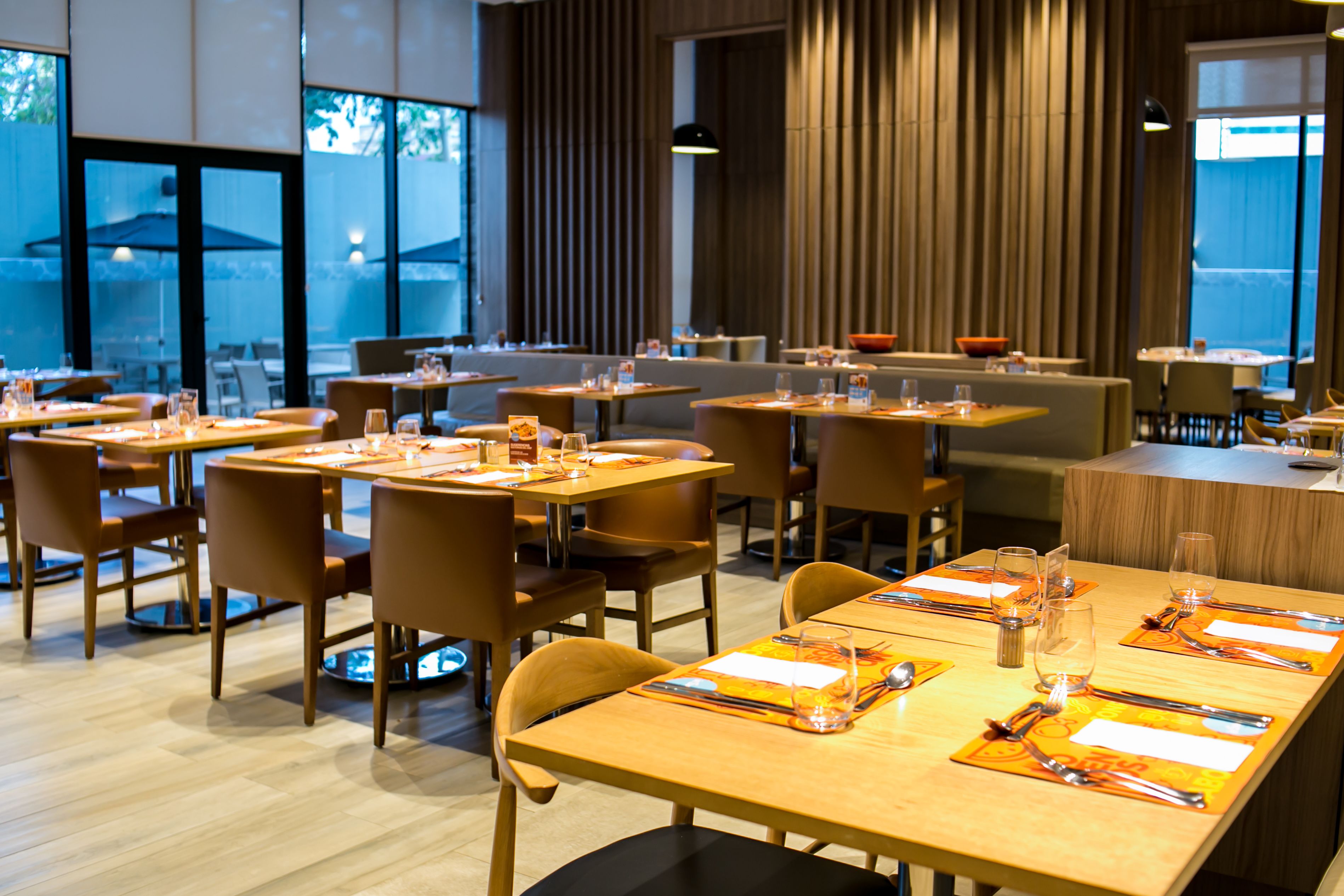 Un restaurante moderno con varias mesas dispuestas para comer, con mobiliario de madera y un diseño limpio y contemporáneo.