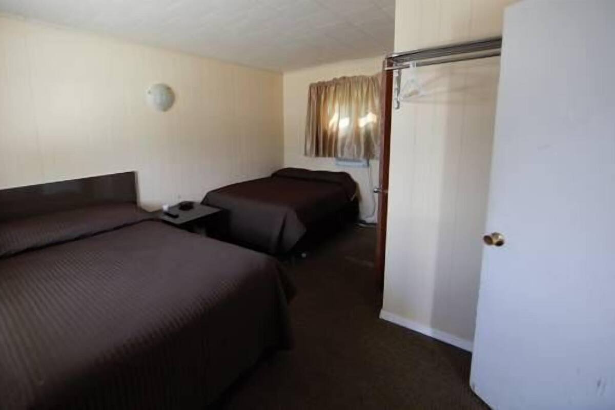 Une chambre d’hôtel avec deux lits, une table de chevet, une armoire et une porte.