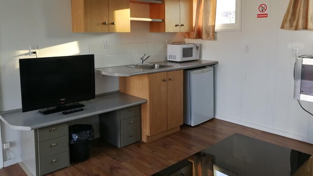 A compact kitchen with wooden cabinets, a microwave, a sink, and a television. - Star Motel (Morden)