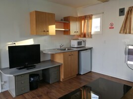 Cocina compacta con armarios de madera, microondas, lavamanos y televisor.
