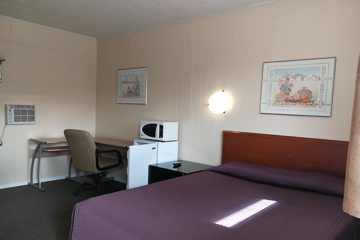 Une chambre d’hôtel équipée d’un lit, d’un bureau, d’une chaise, d’un four à micro-ondes, d’un réfrigérateur et d’un climatiseur fixé au mur.
