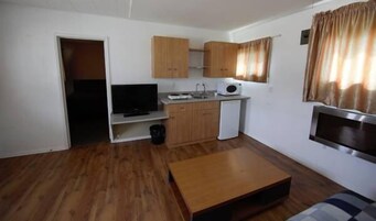 Un espacio habitable compacto con kitchenette, televisor y refrigerador pequeño.